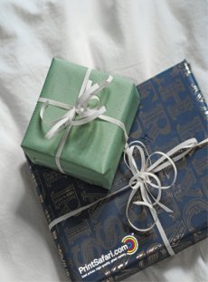 Two wrapped gifts: one in green paper with a white stripe pattern and the other in blue paper with 'Merry Christmas' written in a continuous, repeating pattern.