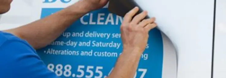 A man applying a blue car magnet on to a white car.