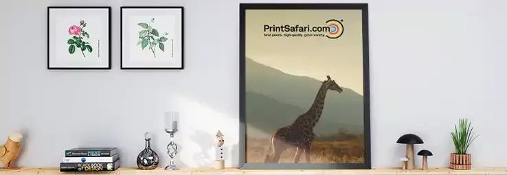 A big framed print next to two smaller square prints on a shelf.
