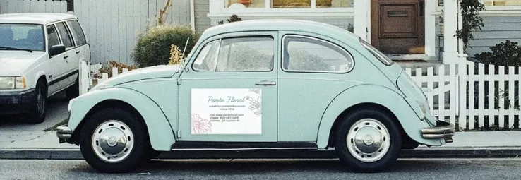A turquoise car on the street with a magnet on its front door.
