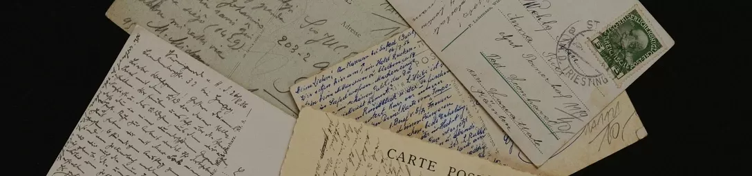 A pile of old handwritten postcards, with a stamped postage mark visible on one of the cards.