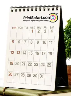 A desk calendar standing on a notebook, in front of a plant .
