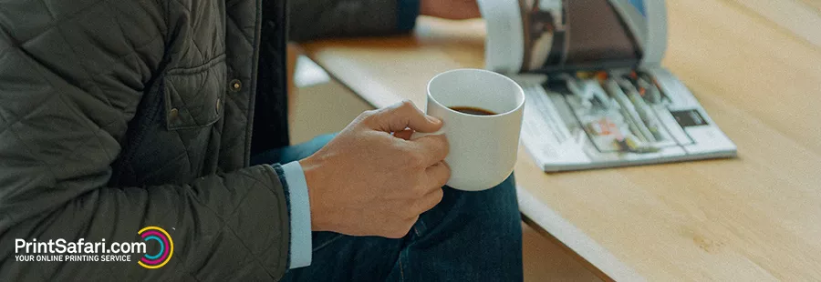 A person holding a cup of coffee in one hand and flipping through a brochure with the other hand.