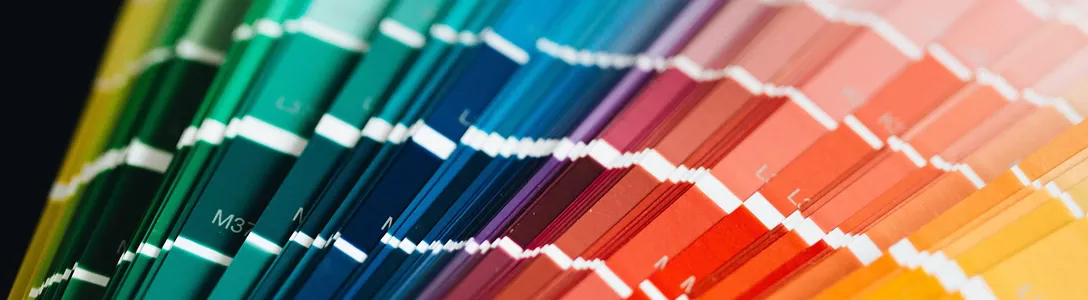 Multiple CMYK Pantone color guides displaying a wide range of colors - from dark green on the left, transitioning through blue, purple, and red, to orange on the far right.