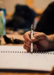 Hand holding a pen over a spiral notebook.