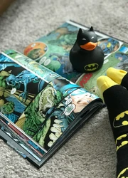 A comic book lying on the floor with feet visible next to it.