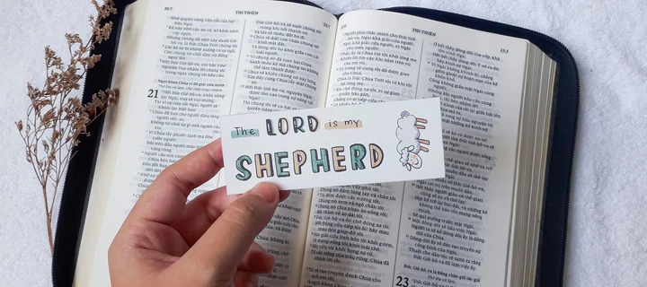 A bookmark held by a hand on top of an open book.