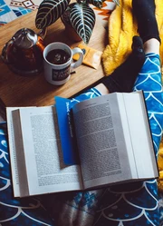 Book with a blue bookmark inside laying on the legs of a human