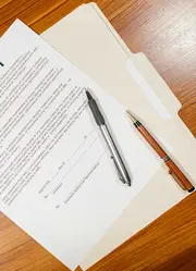 A presentation folder on a wooden table with a document and pens on top.