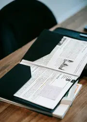 A black presentation folder on a wooden table with documents inside.