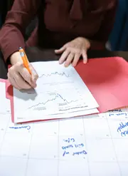 Hands drawing a graph on a document inside a presentation folder.