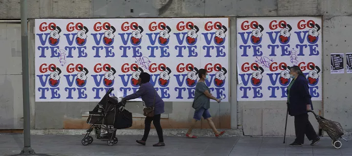An outdoor wall showcasing many posters, with white background and blue and red text.