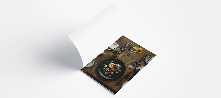 Open cookbook on the first page, showing a white inside cover and the first page with a picture of a table set with plates, flowers, and a meal on a plate.