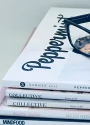 Reading glasses resting on a stack of neat white magazines.