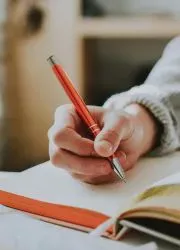 Close-up of student writing in a workbook with red pen, showcasing the practical use of learning materials