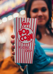 A woman holding a popcorn box towards the camera
