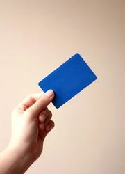 A hand holding a blue plastic card in front of a beige wall.