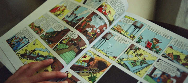 Close-up of a boy's hand turning the page of a comic book, with only the book and one hand visible.