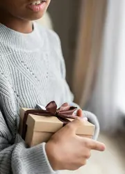 A person holding a cardboard box in their arms, decorated with a ribbon