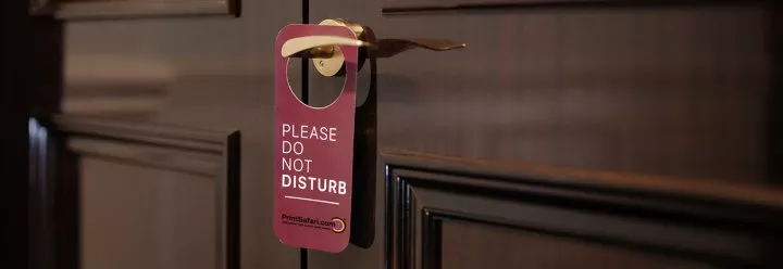 Hotel room door with a red 'Do Not Disturb' door hanger hanging on the handle.