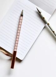 An open notepad with two ballpoint pens on it