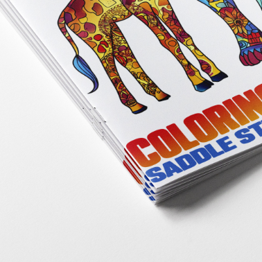 Close-up of stacked coloring books showing colorful giraffe artwork and bold title text on the cover.