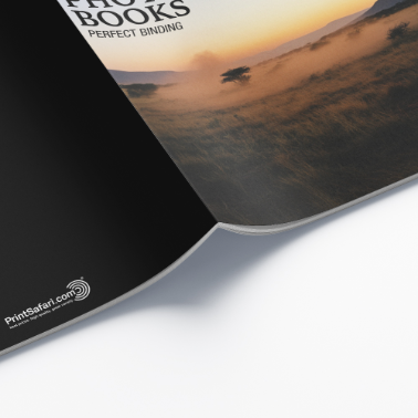 Close-up of an opened photography booklet displaying the cover with an orange sunset and elephant, revealing the first black inner page.