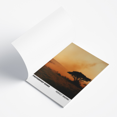 Opened photography booklet showing a full-page image of an elephant at sunset, laid flat on a white surface.